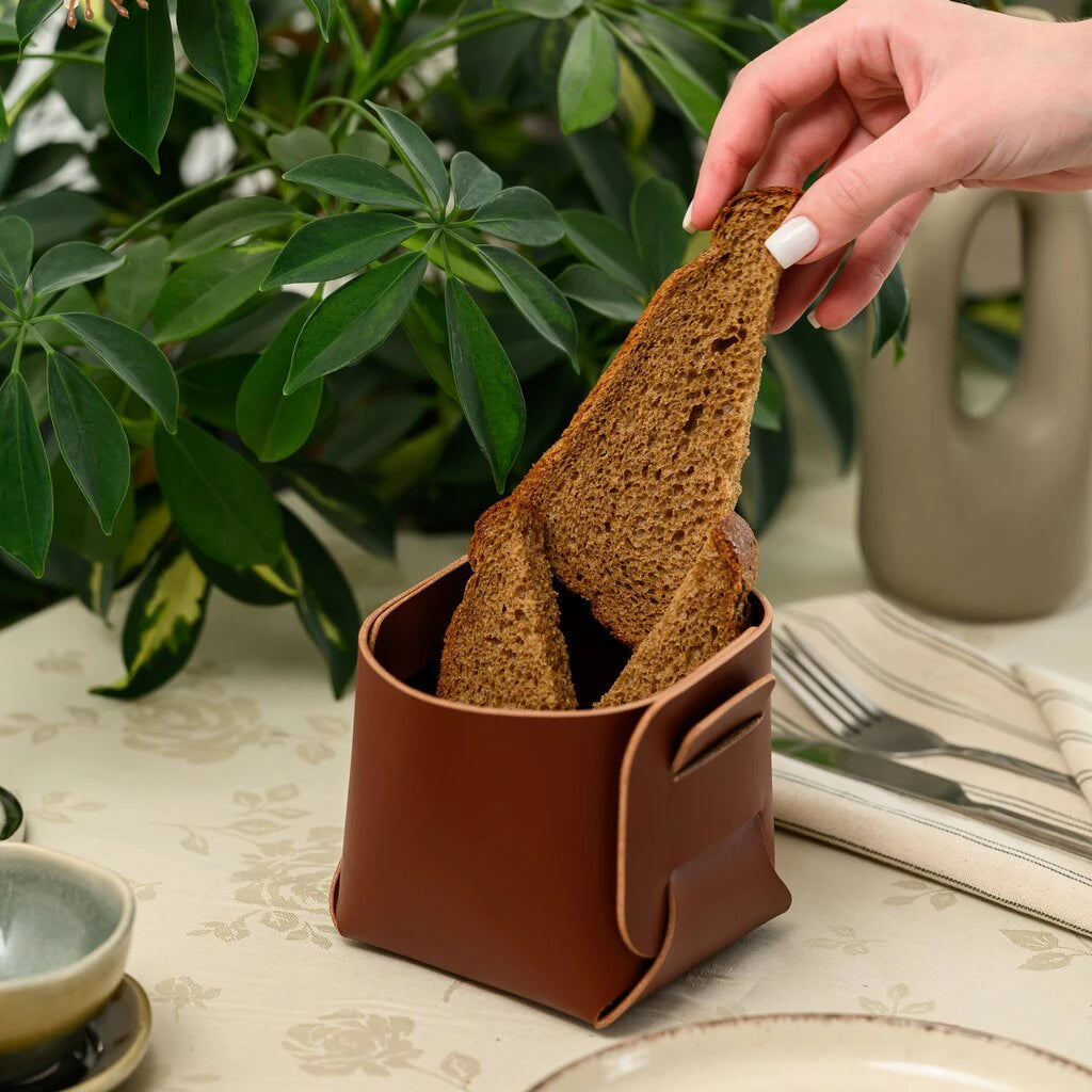 Elegant home serving: a handcrafted leather bread basket being filled with fresh bread, showcasing its compact design and premium aesthetic
