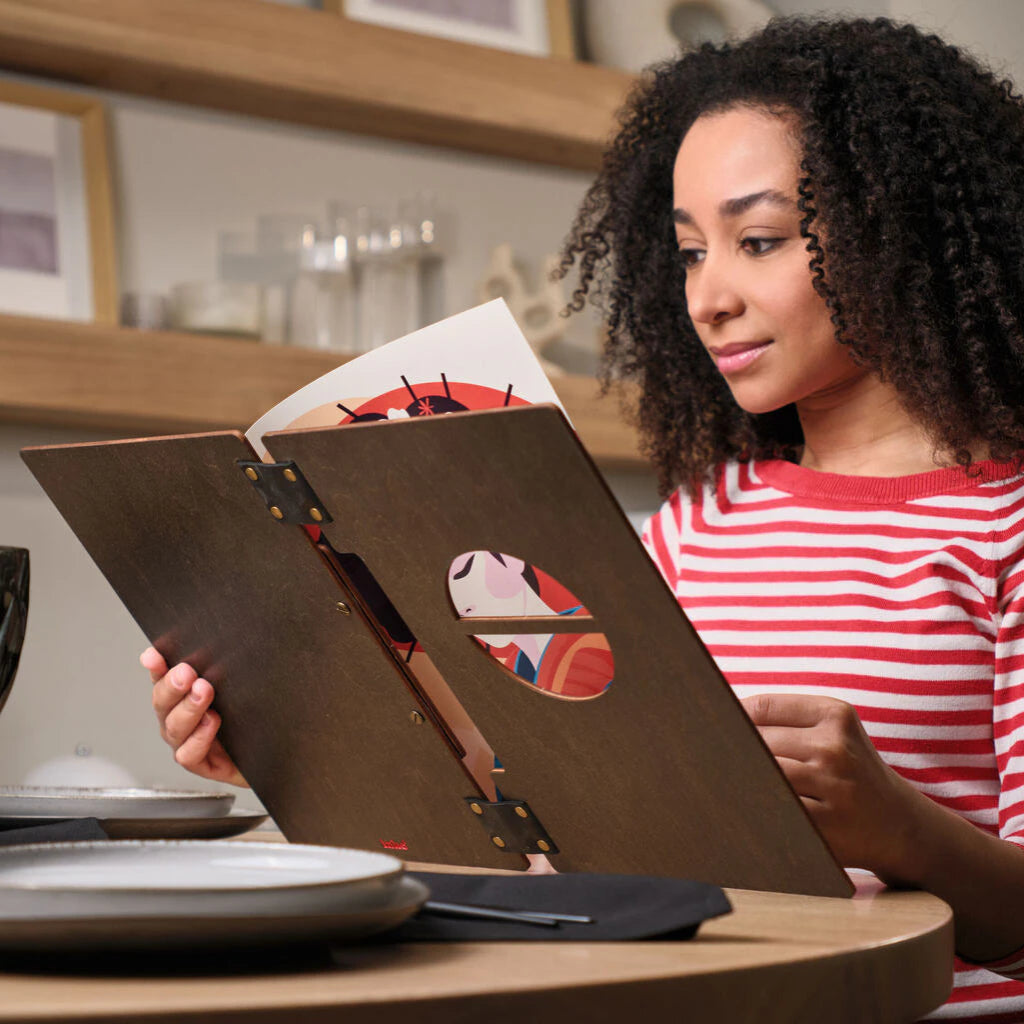 A girl in a striped sweater browses a wooden menu in a restaurant, holding it with both hands