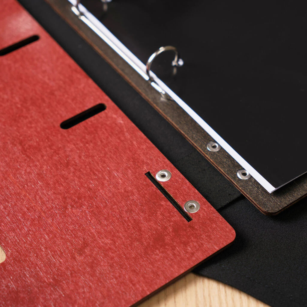 Detailed close-up of the ring binder mechanism and the silver rivets on the chili-red wooden cover and dark inner page