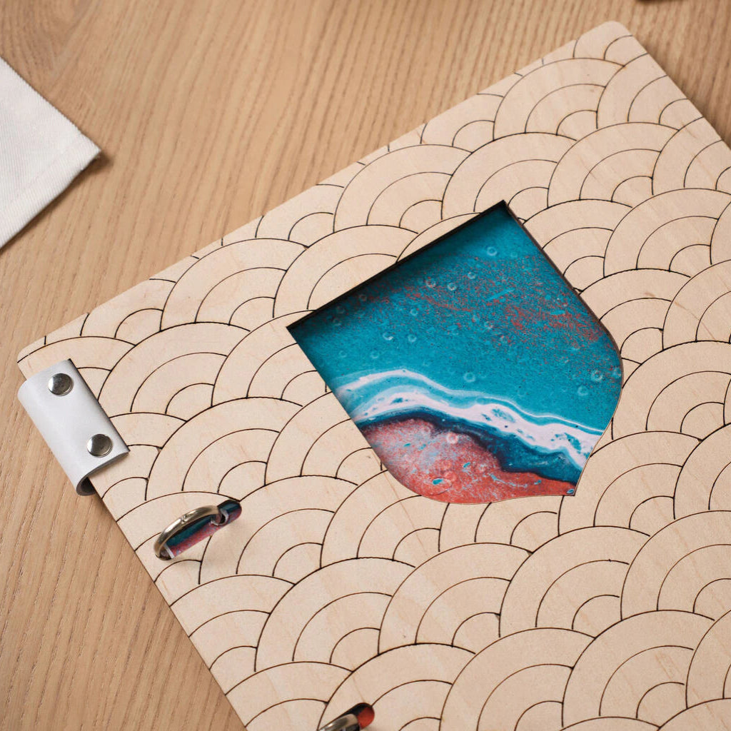 Macro close-up of the wave pattern on light wood menu cover, showcasing the shield-shaped geometric cutout with vibrant printed ocean art inside.