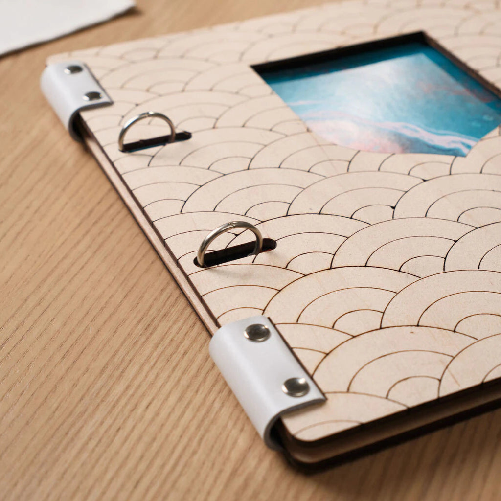 Side angle view of light wood menu binder showing detailed wave pattern, chrome binder rings, and white leather straps from a different perspective.
