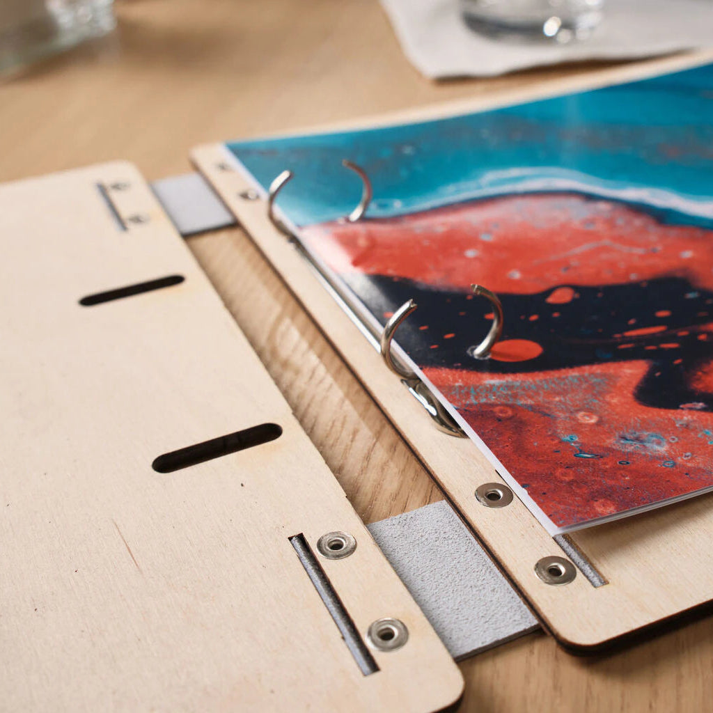 Close-up of the internal structure of an open light wood binder, showing the ring binders with printed ocean art and precise metal fasteners.