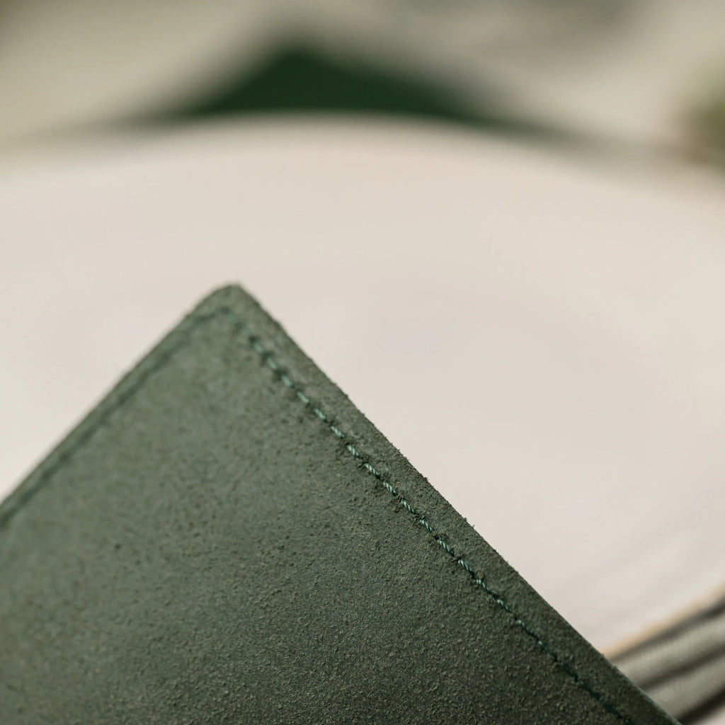 Macro close-up of a square forest green leather placemat corner, showcasing the high-quality tonal stitching and soft, velvety suede-like texture for a luxury finish