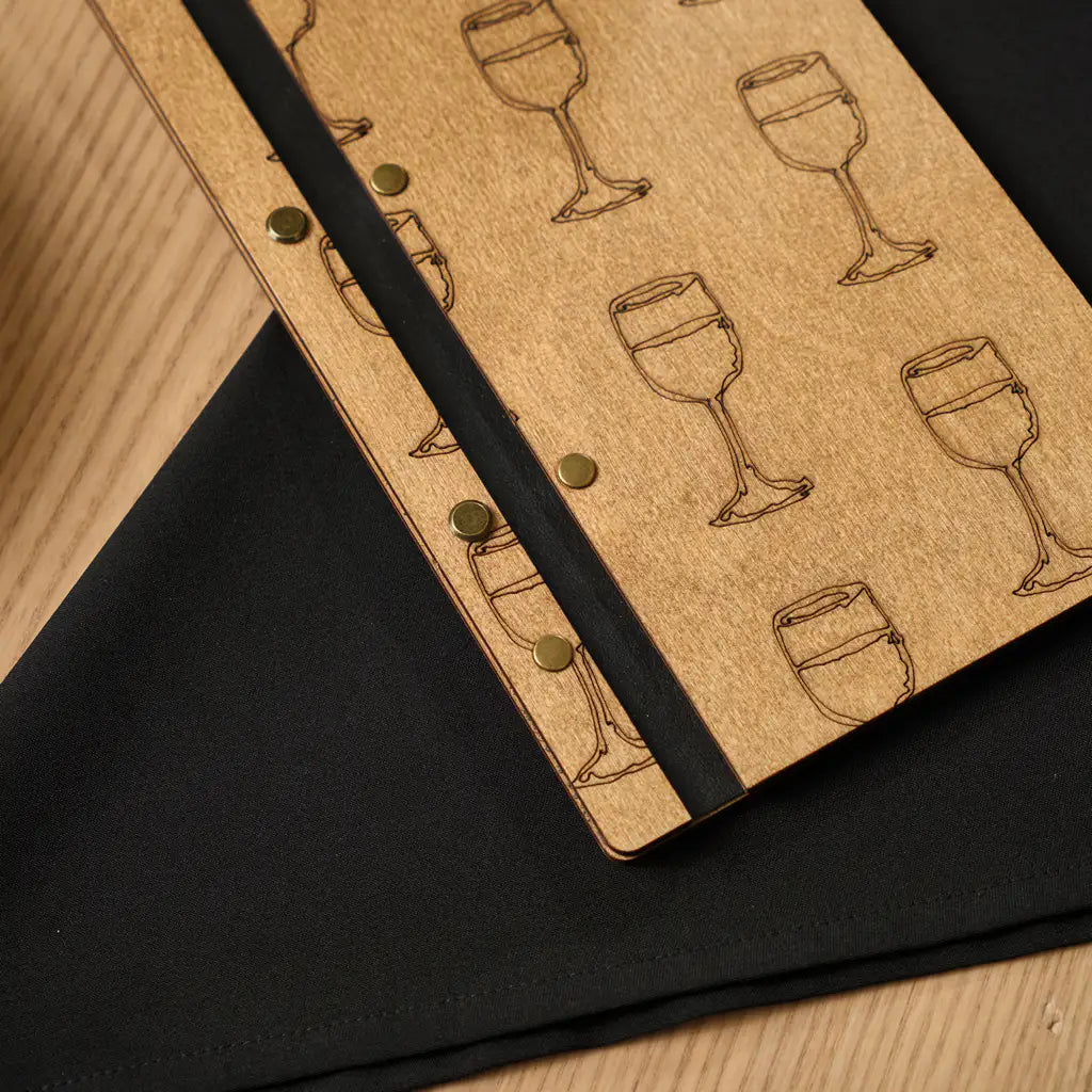 A macro shot of the menu’s binding and front cover, showcasing the texture of the engraved wine glass illustrations and the antique-style brass rivets.