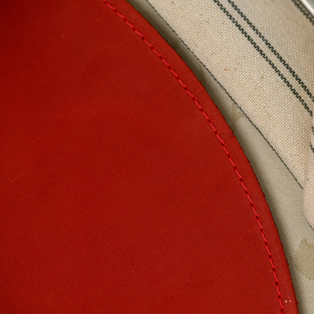 Extreme close-up of the precision edge stitching on an oval red leather placemat, showing the high-quality durable finish