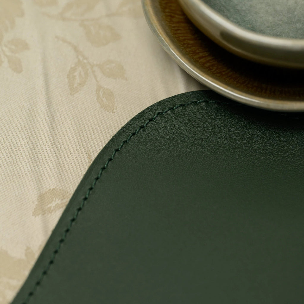 Premium forest green scalloped leather placemat with professional edge stitching, paired with elegant ribbed dinnerware and floral textiles