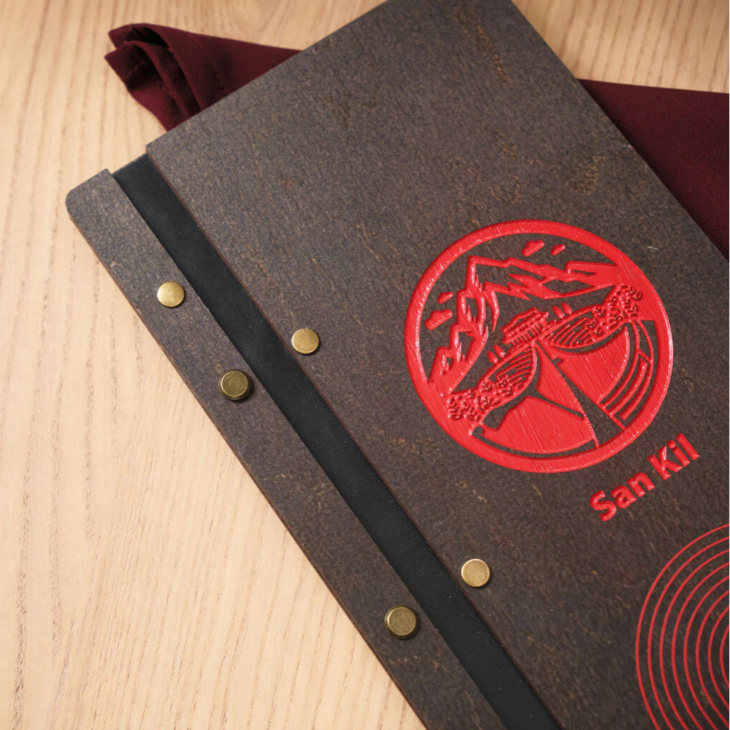 : A close-up view of the menu's top half, highlighting the deep red, intricately engraved circular logo featuring mountains and the "San Kil" name against the dark wenge wood grain.