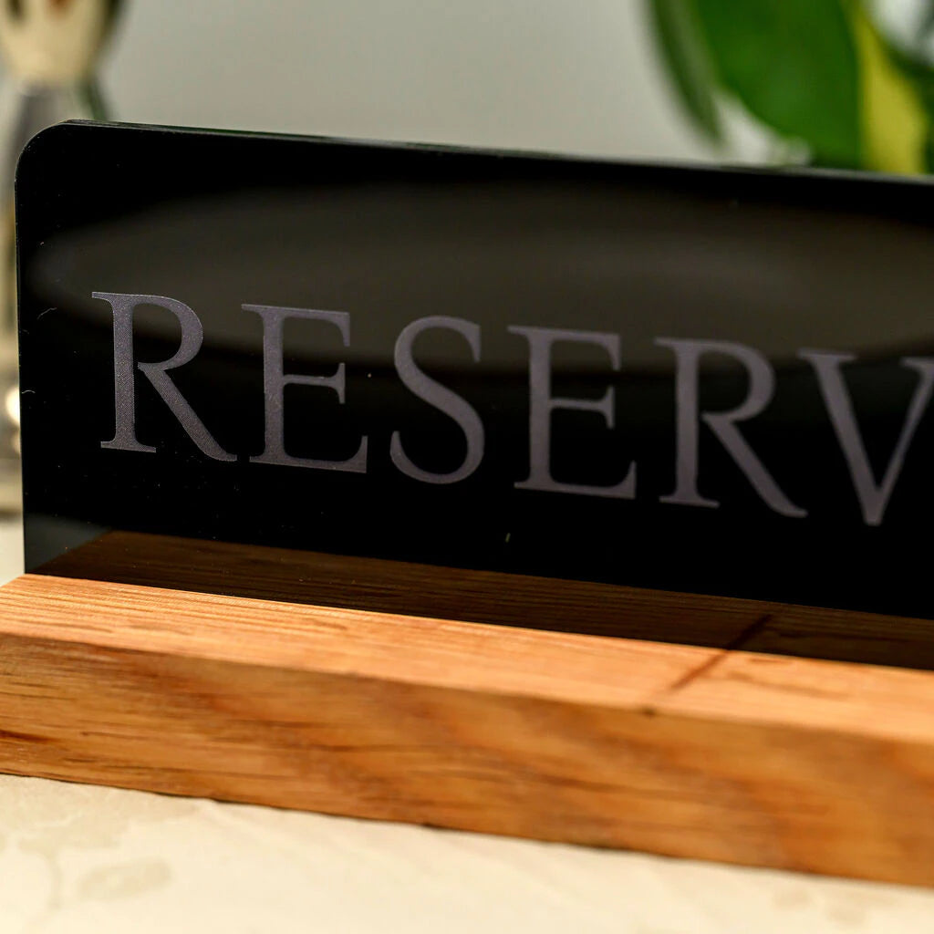 Close-up of a premium reserved table sign featuring laser-engraved lettering on black acrylic with a solid oak wood base