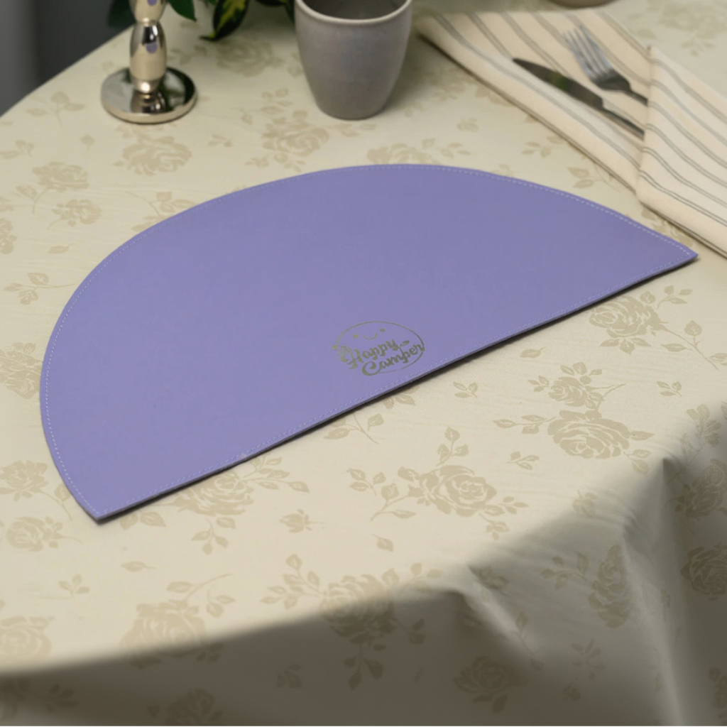 Wide shot of a table setting featuring a lavender leather placemat, a grey plate and bowl, and a neutral-toned floral tablecloth