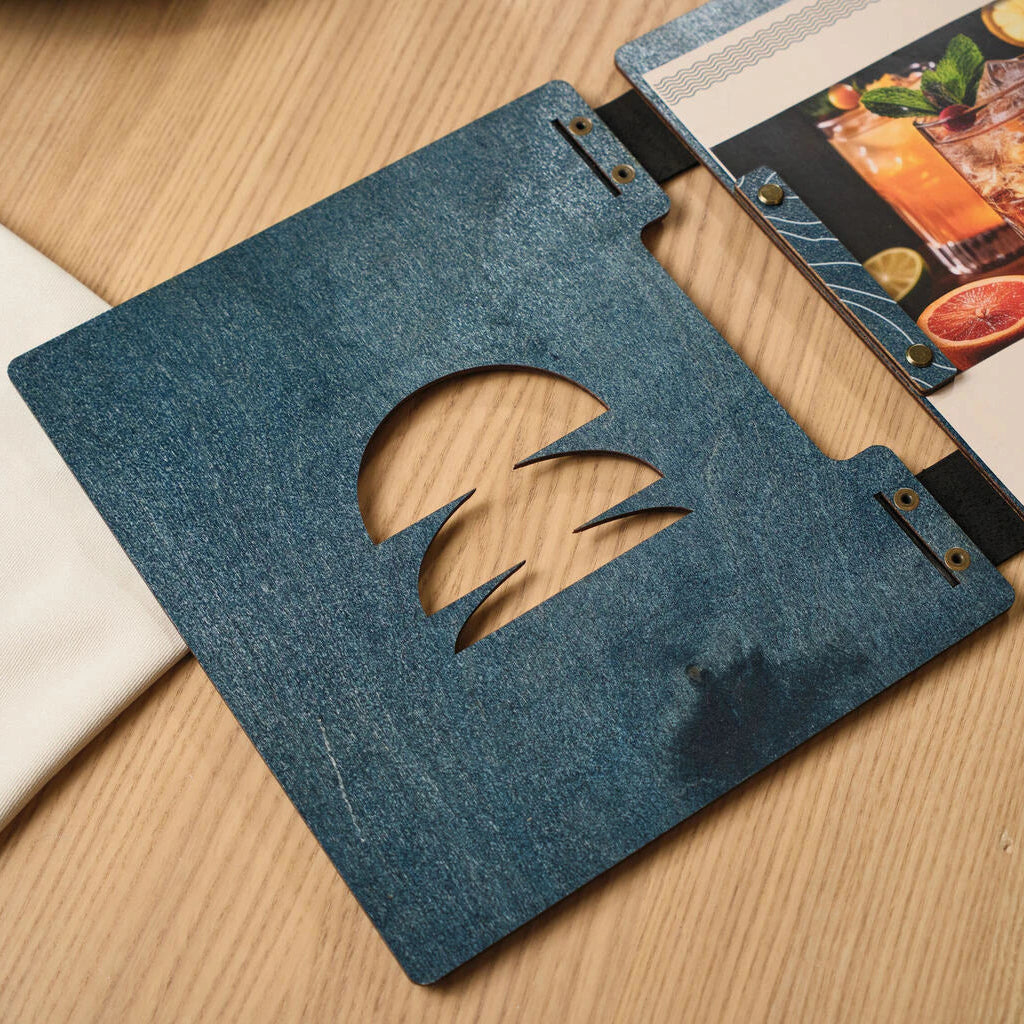 Inside view of a custom restaurant menu holder made of blue wood and leather, lying open on a wooden table with dining glassware