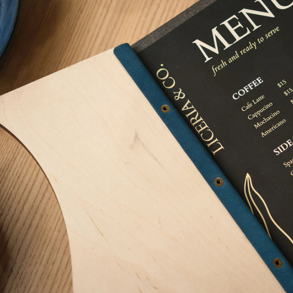 Close-up of the internal binding of a premium wood menu, highlighting the contrast between the light wood grain, the blue textured spine, and the gold-lettered menu insert