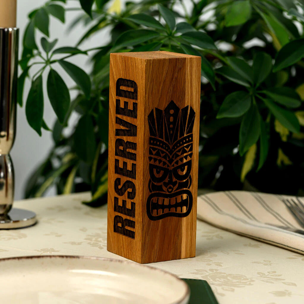 Solid oak wood reservation block with high-quality laser engraving. The natural wood grain is clearly visible, highlighting the premium finish. The vertical design and unique Tiki-style mask engraving make it an ideal accessory for themed bars, lounges, or tropical restaurants