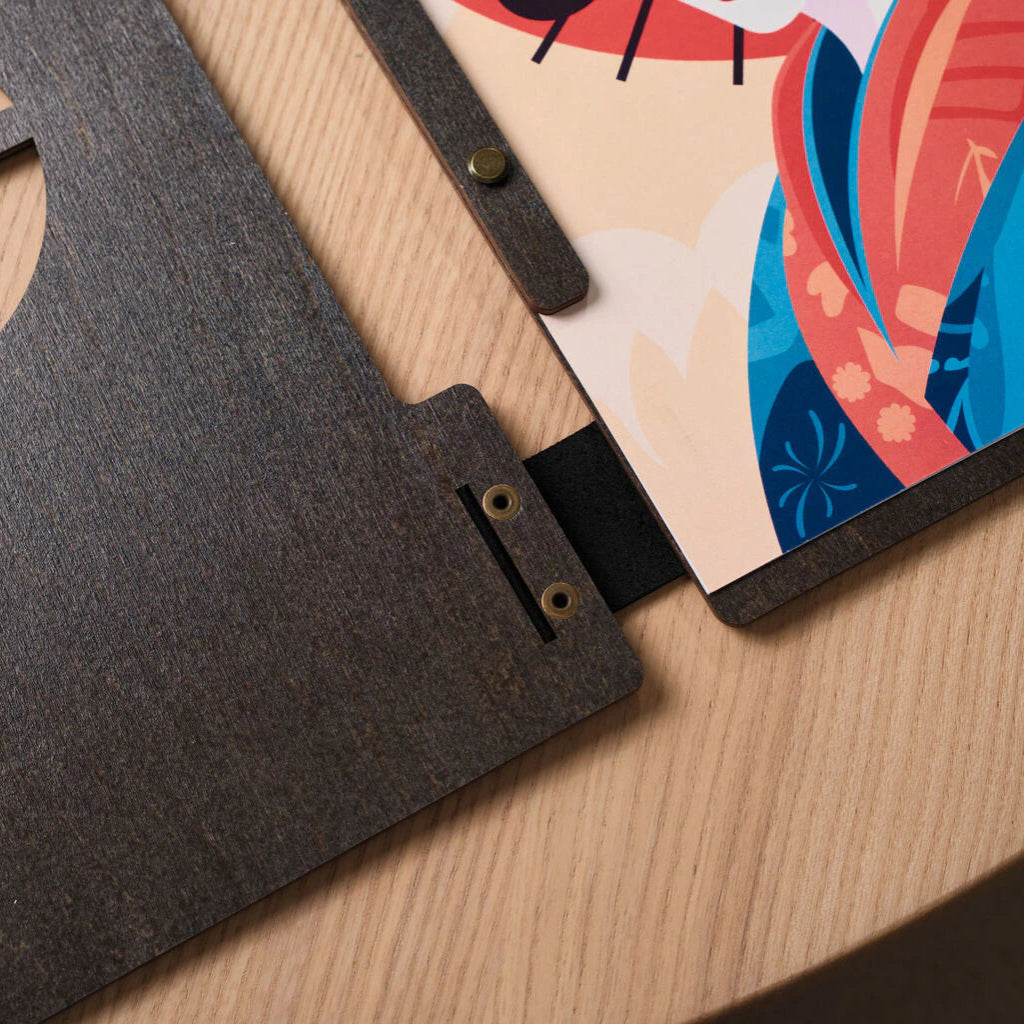 A close-up showing the internal binding mechanism: a black leather strap connects the wooden panels through reinforced metal eyelets, with a wooden strip holding the internal pages in place.