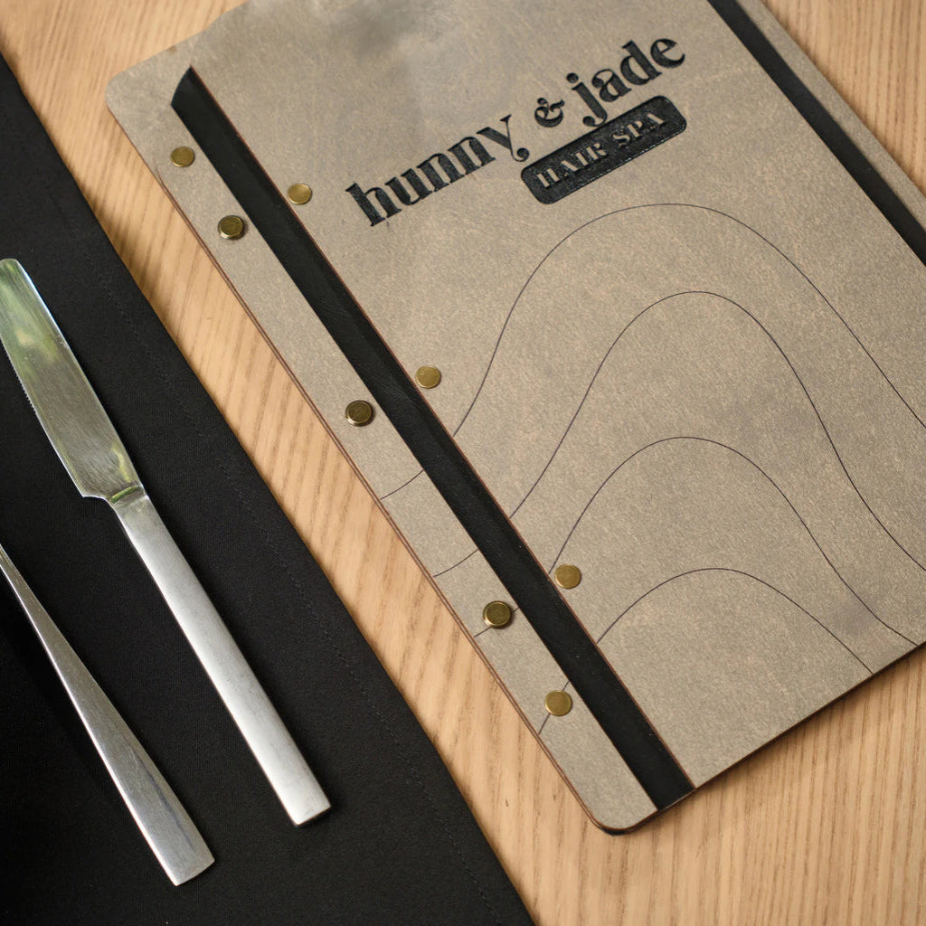 Minimalist engraved wave pattern on a professional gray wood menu cover, highlighting custom design for hospitality and beauty businesses