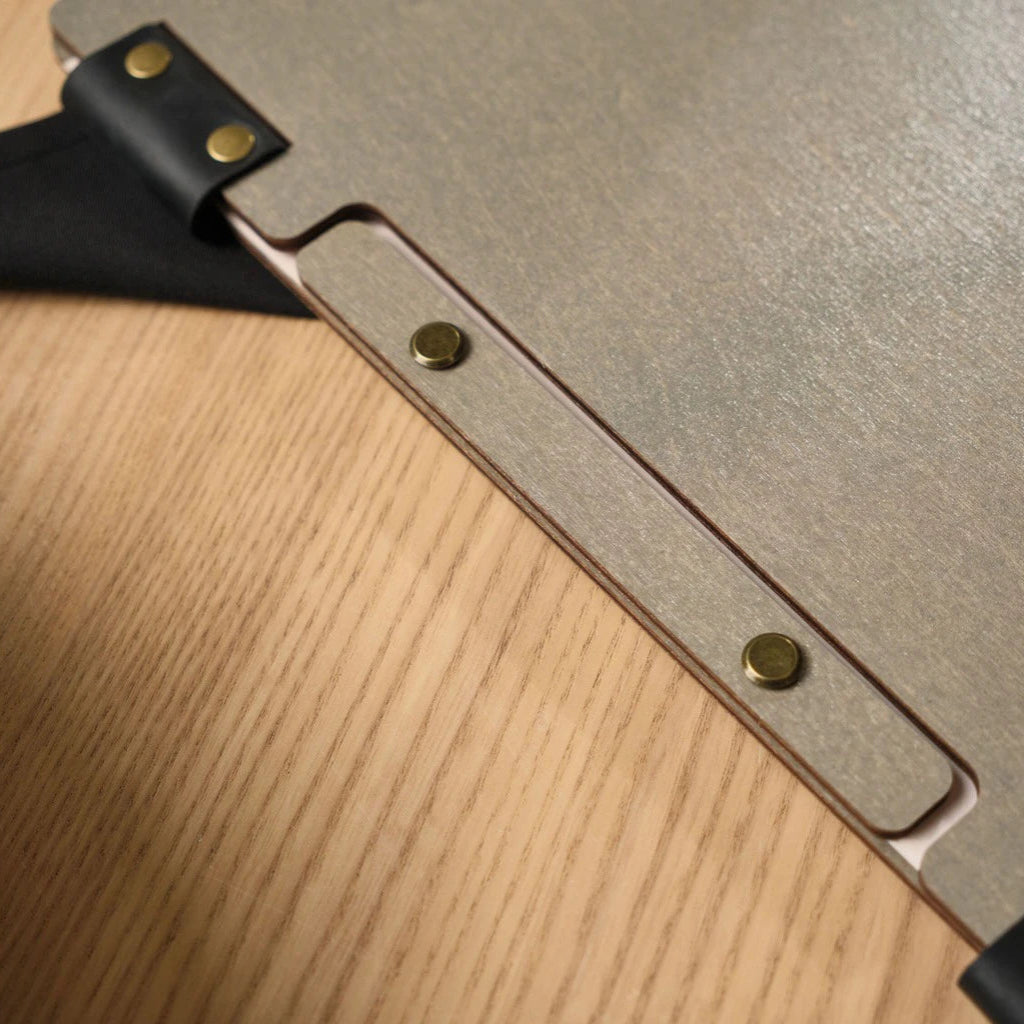 Extreme close-up of a grey wooden menu folder showcasing the unique leather strap binding and bronze metal rivets. This handcrafted wood menu cover highlights the precision-cut recessed spine and premium textured finish for professional restaurant use