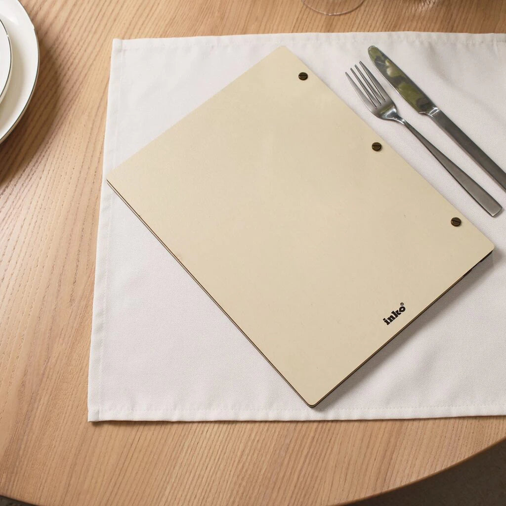 Wooden menu cover with brass screws by Inko on white linen napkin with fork and knife on wooden table