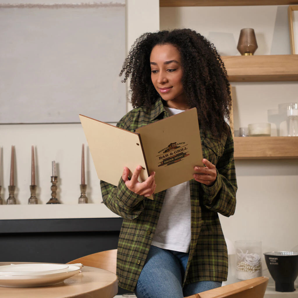Woman reading open wooden menu cover with Bar & Grill branding in modern dining room interior