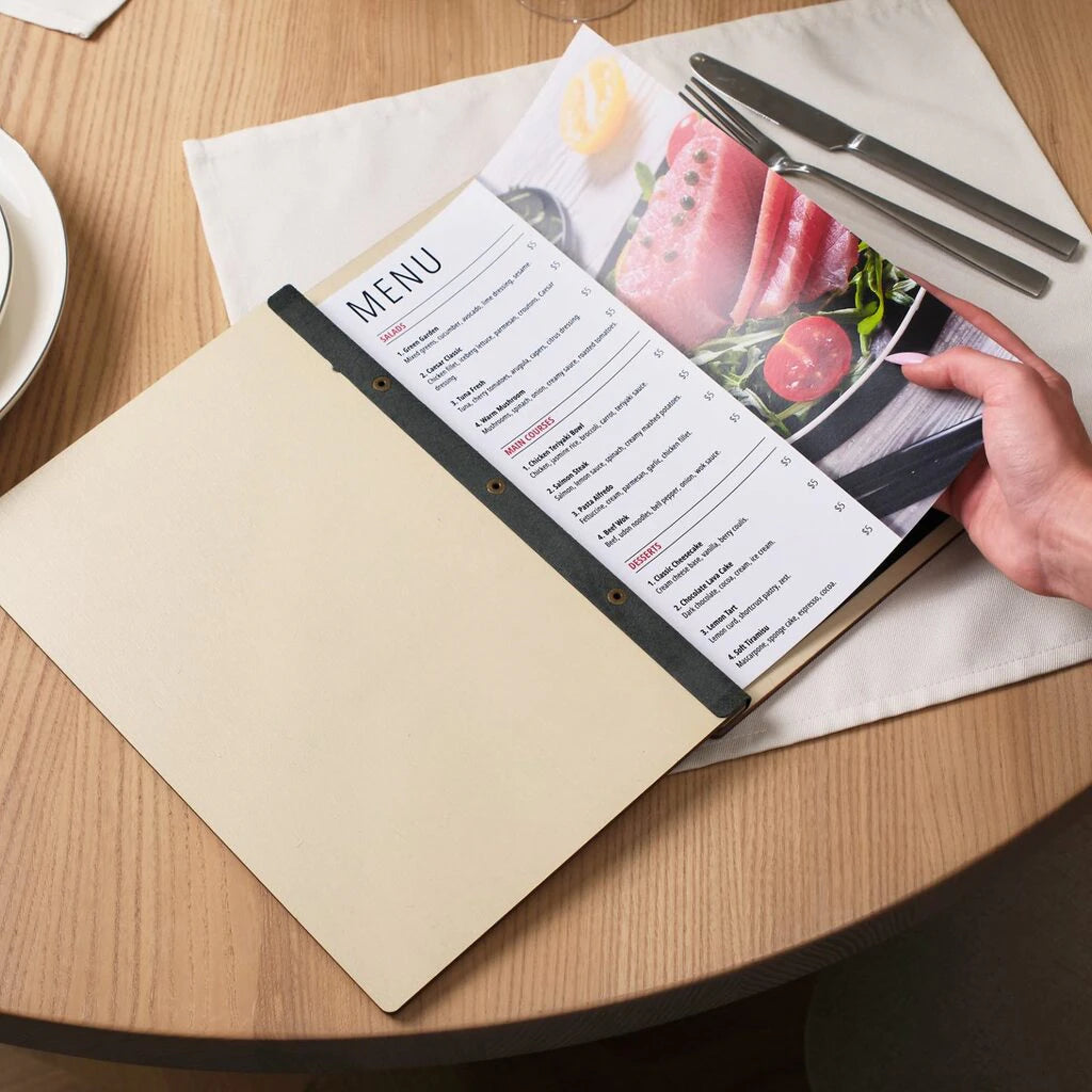 An open light wood menu holder being held by a customer in a restaurant setting. The folder features natural birch panels connected by a flexible black leather spine with three brass-tone screw posts. This internal bolt-binding system securely holds a full-page menu with vibrant food photography