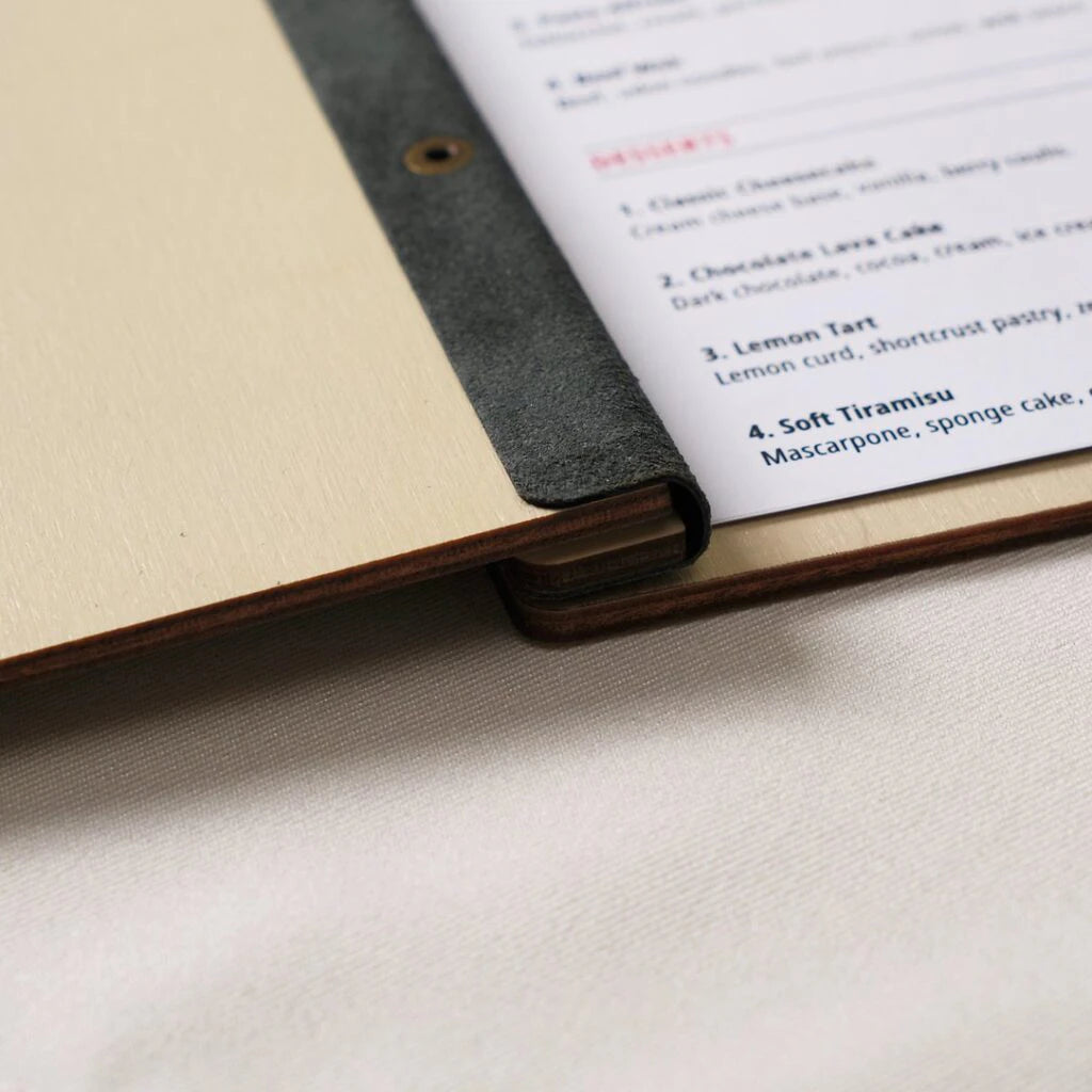 Close-up of wooden menu cover spine with black leather binding and printed dessert menu page inside