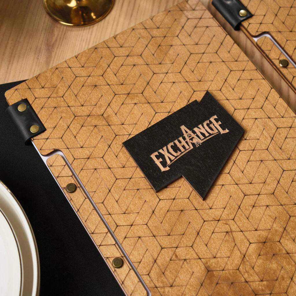 Close-up of a natural wood menu cover with an intricate laser-engraved pattern and a contrasting black logo