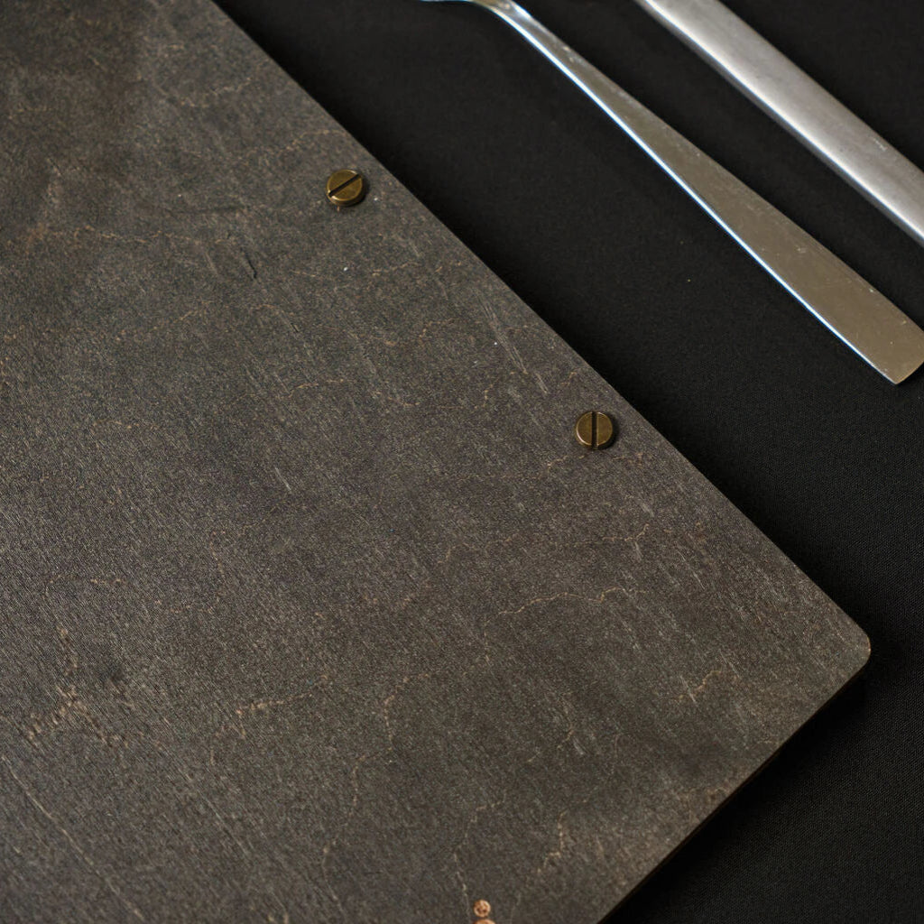 Macro shot of the back of a natural oak wooden menu folder, showing the dark wood texture and gold screw post fasteners