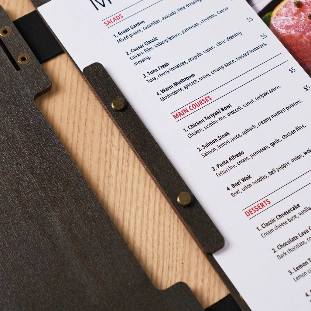 A detailed close-up of an open wenge wooden menu, showing the internal wooden strip that secures the paper menu using brass screws. The printed menu list features categories for Salads, Main Courses, and Desserts.