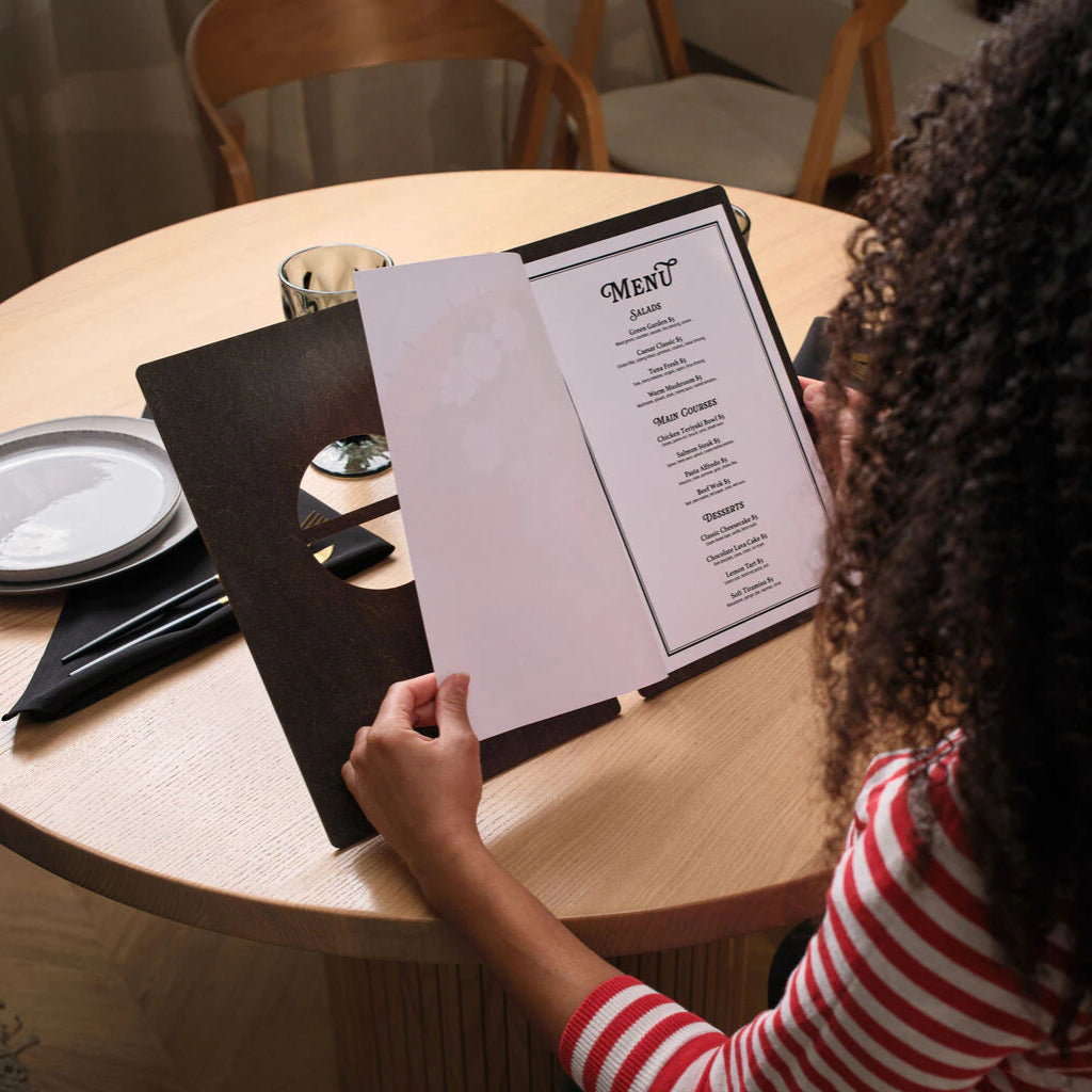 A customer holding the open menu over a table, showing the printed content.