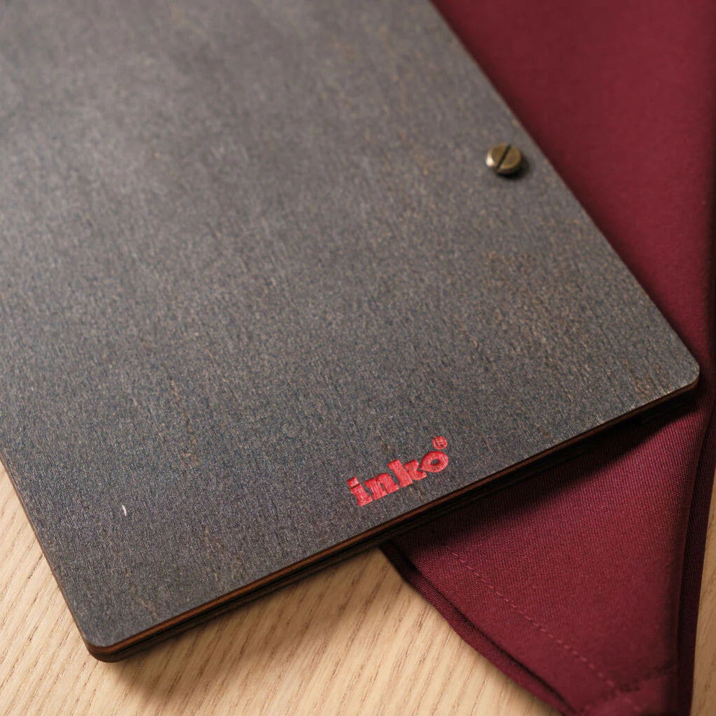 A close-up of the bottom corner of the back cover, featuring a small, vibrant red "inko" brand logo printed on the dark wood grain.