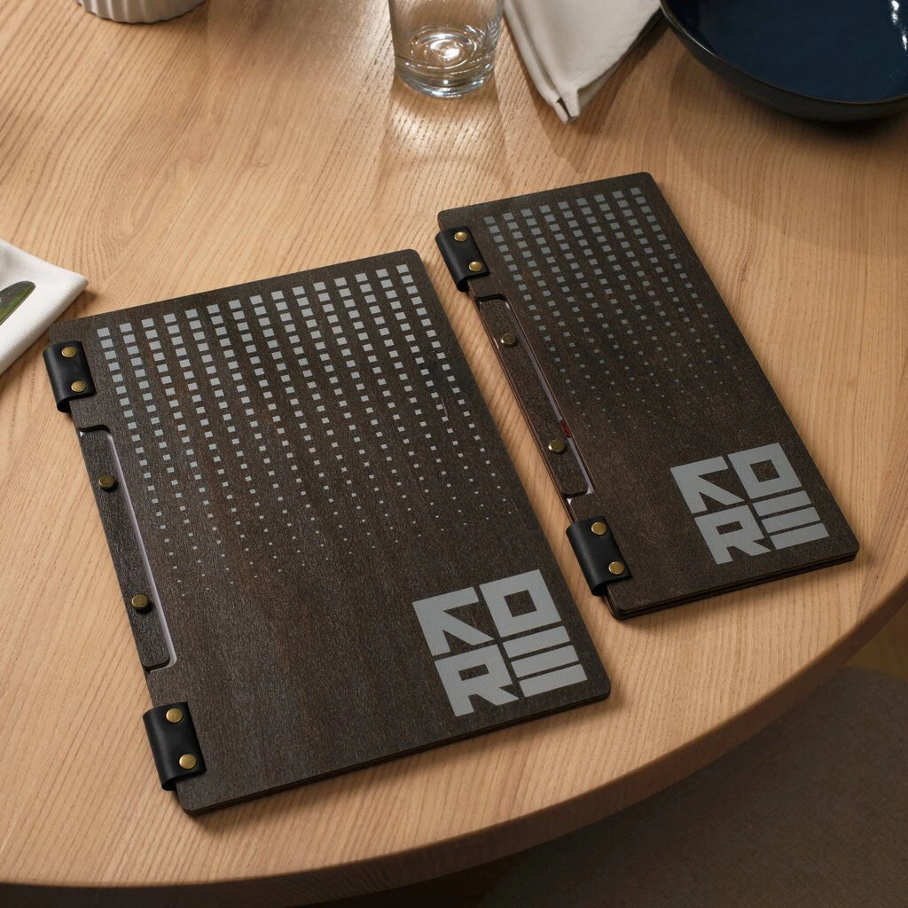 A comparison of two handcrafted wooden menu covers, focusing on the narrow, compact folder designed for specialty lists. Made from dark-stained wood with natural leather accents, this slim menu holder stands out for its unique shape and professional laser-engraved branding, ideal for bars and cafes