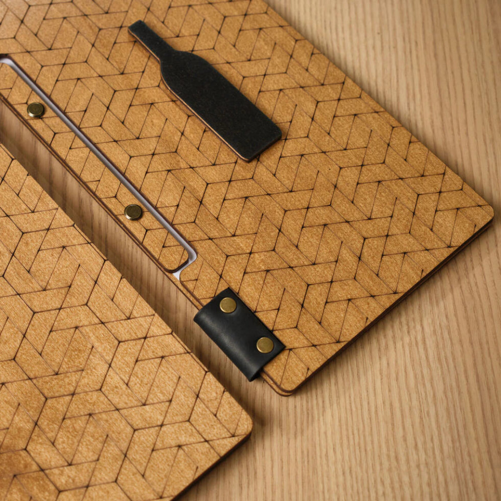 A close-up of the oak-colored menu folder, highlighting the detailed laser-engraved geometric pattern of interlocking hexagons and a black decorative bottle-shaped inlay.