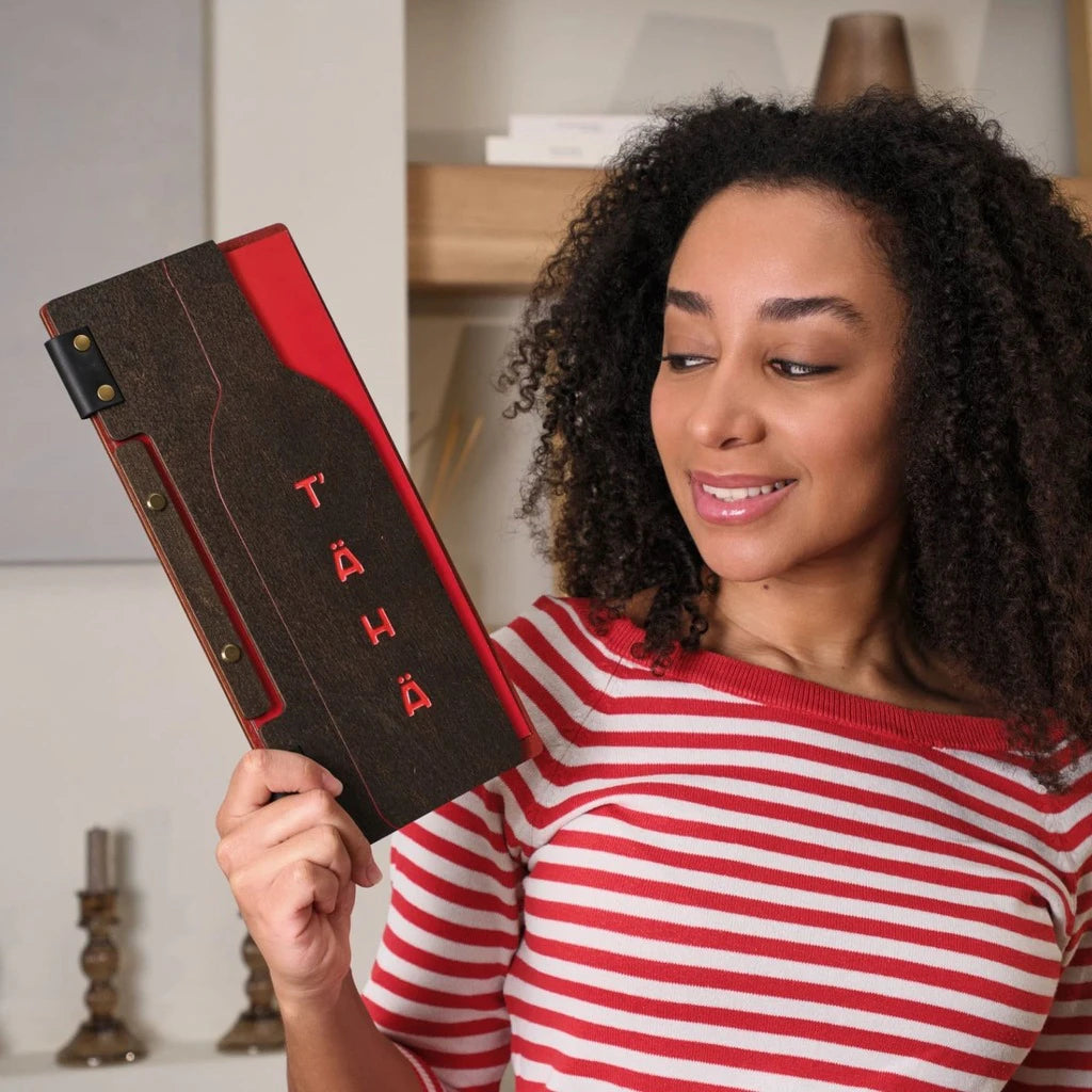 A woman holding a custom wooden menu folder with a unique wine bottle cutout and red color engraving. This handcrafted wood menu cover features black leather hinge details and professional bolt binding