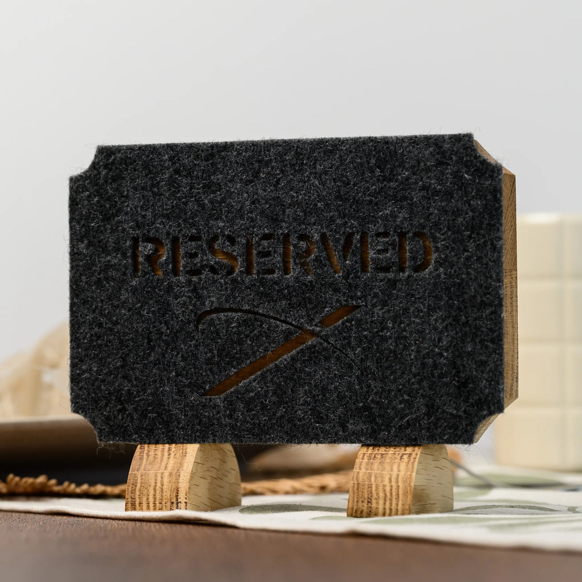 Дубова табличка «Reserved» з прорізаним фетром на сервірованому столі, крізь прорізи напису й логотипу проглядає світлий дуб