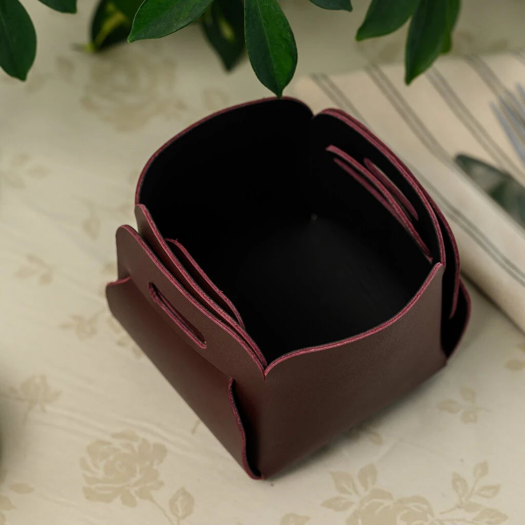 An empty dark burgundy leather bread basket with a square, interlocking tab design, shown in a cozy kitchen setting