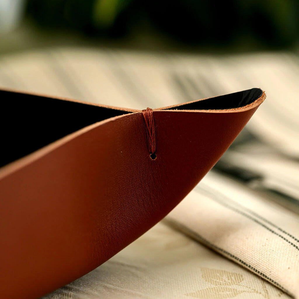 Close-up of a handcrafted leather bread basket corner, showcasing the meticulous hand-stitched detail and the premium texture of the brown genuine leather. The interior features a sleek black lining, highlighting the artisan quality and durable construction of this restaurant table accessory