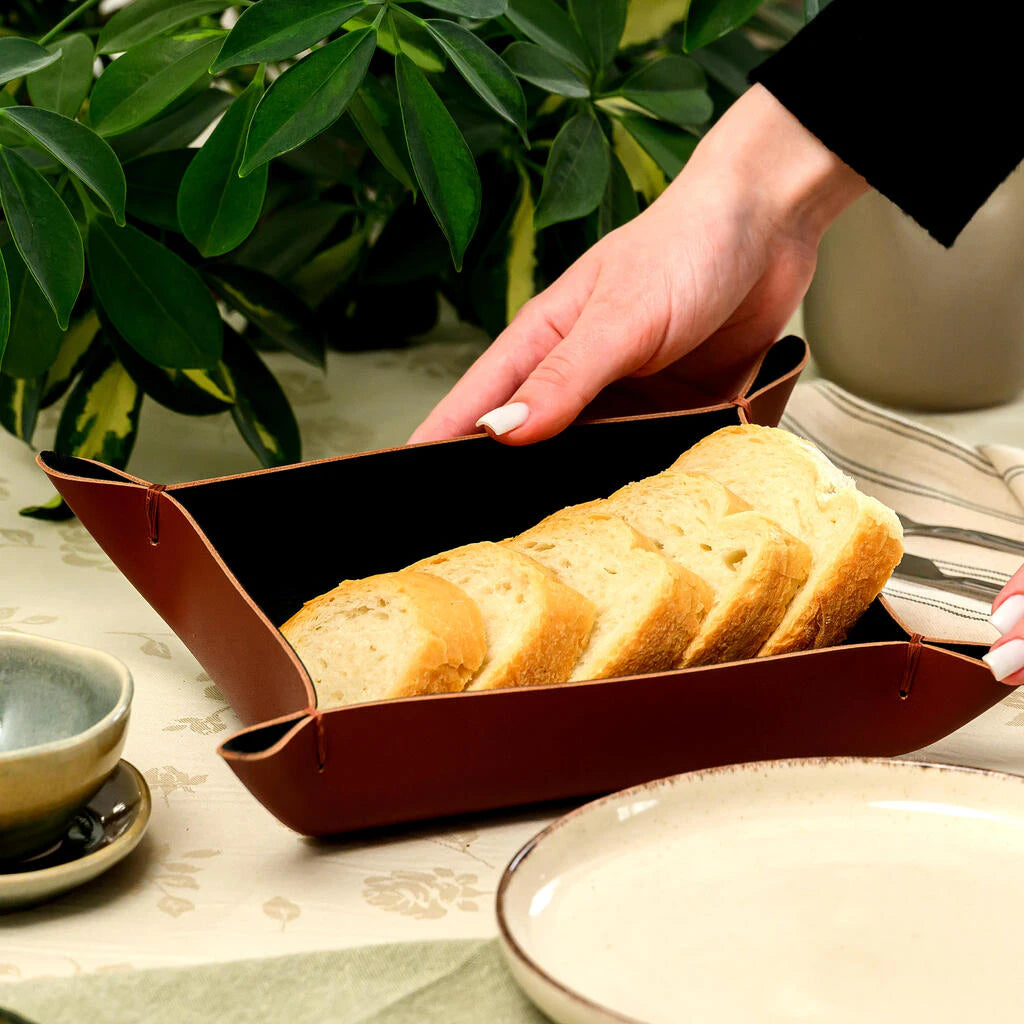 Brown leather bread basket filled with fresh bread slices. This functional table-top accessory features a unique folded corner design, shown in a clean dining setting to highlight its premium look for modern hospitality branding