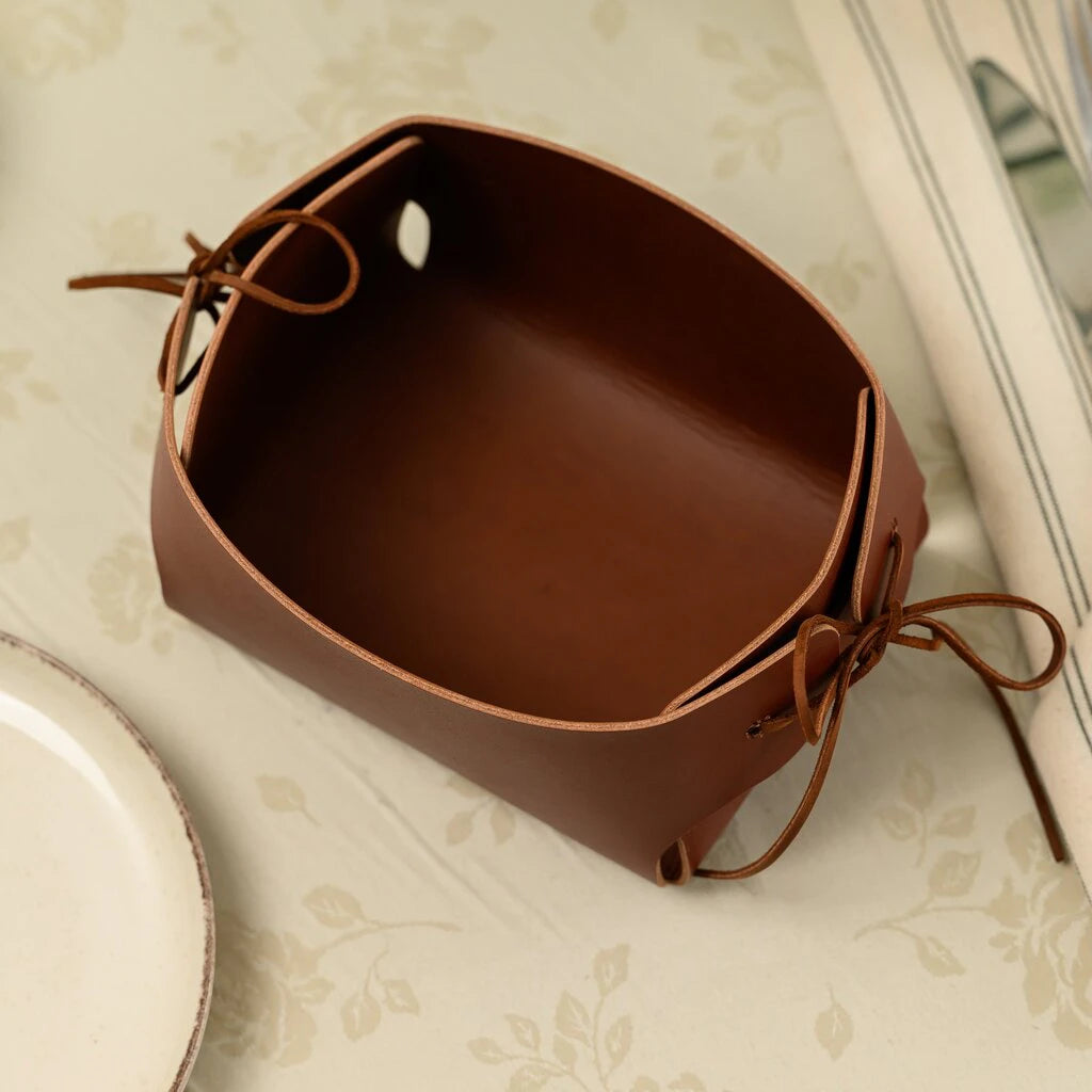Empty brown leather bread basket with adjustable leather ties on the sides, showing its unique deep box shape and premium smooth texture