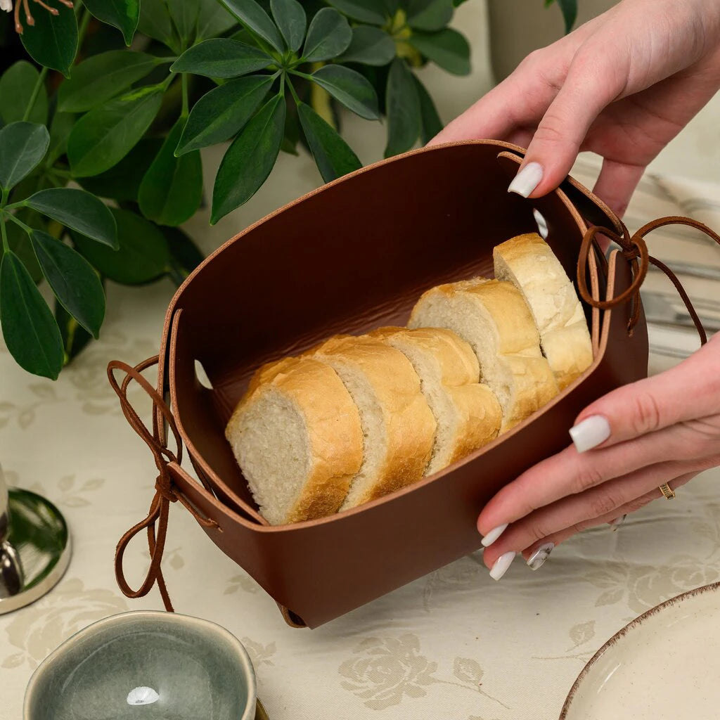 Person holding a handcrafted brown leather bread basket with adjustable leather lace ties, showcasing the unique foldable design and premium texture