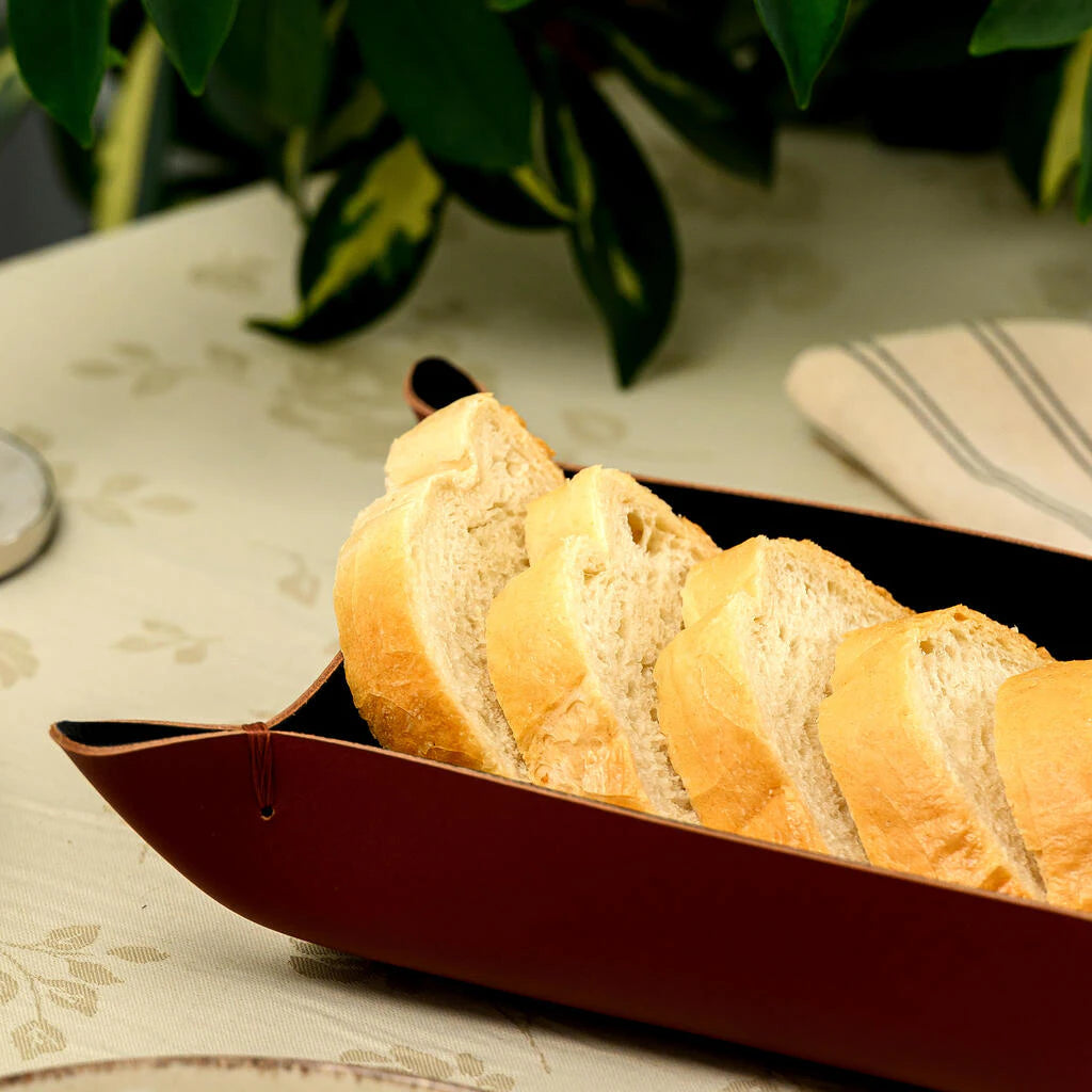Slices of crusty white bread arranged in a stylish deep red leather bread basket on a patterned tablecloth
