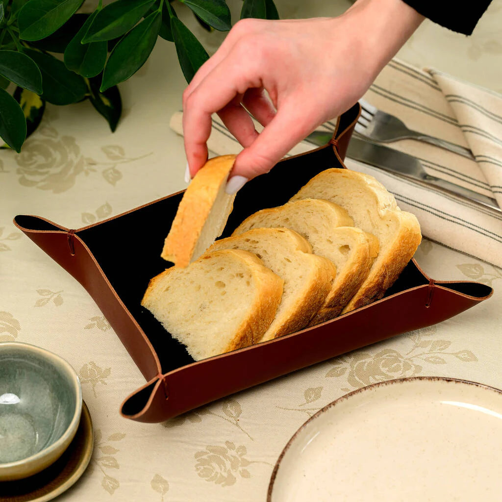 Premium genuine leather bread bowl in a deep tan color. This artisan table accessory features decorative corner stitching and is shown filled with sliced bread, highlighting its practical size and elegant rustic style for professional hospitality use