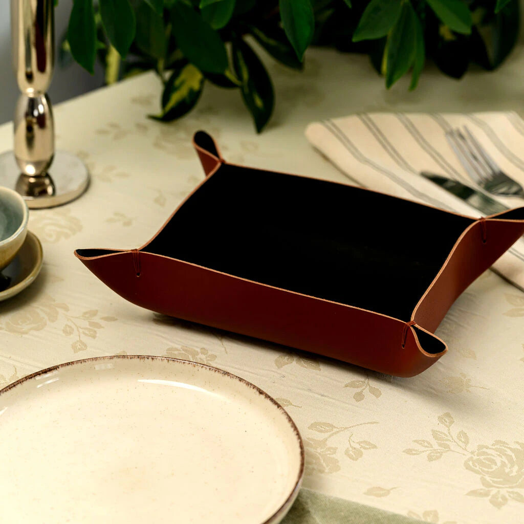 Handcrafted rectangular bread basket made of rich brown genuine leather, filled with fresh baguette slices. The basket features unique folded and stitched corners with a black interior, elegantly placed on a restaurant table
