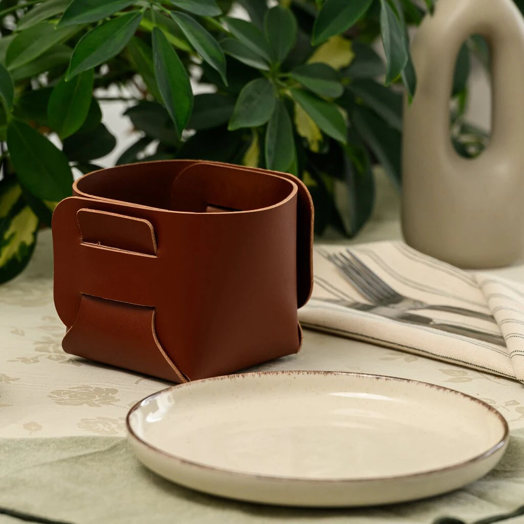 Top-down view of an empty square brown leather bread basket on a floral tablecloth.