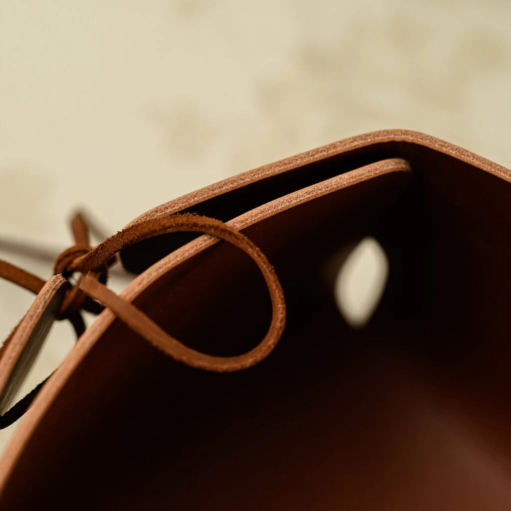 Extreme close-up of a brown leather bread basket showing the high-quality raw edge finish and a durable leather tie knot.