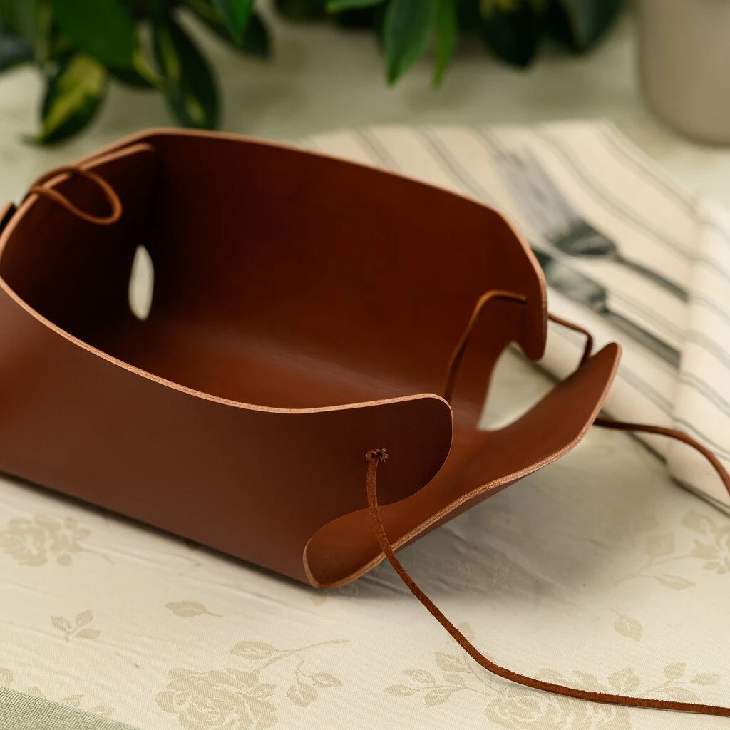 Semi-assembled genuine leather bread bin on a table with cutlery, highlighting the minimalist construction and adjustable leather cord fasteners