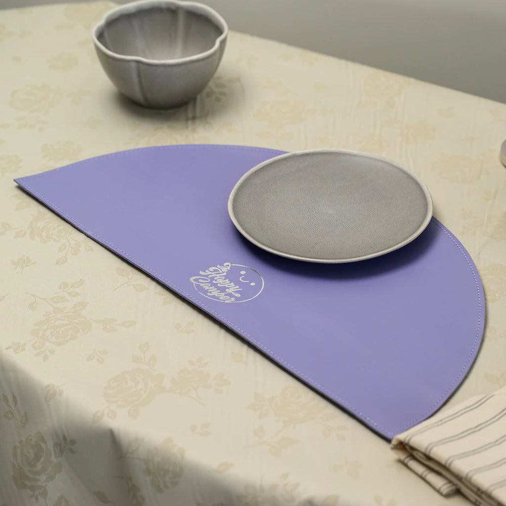 Perspective view of a lavender semi-circular placemat on a table, highlighting its unique curved shape and the elegant silver branding