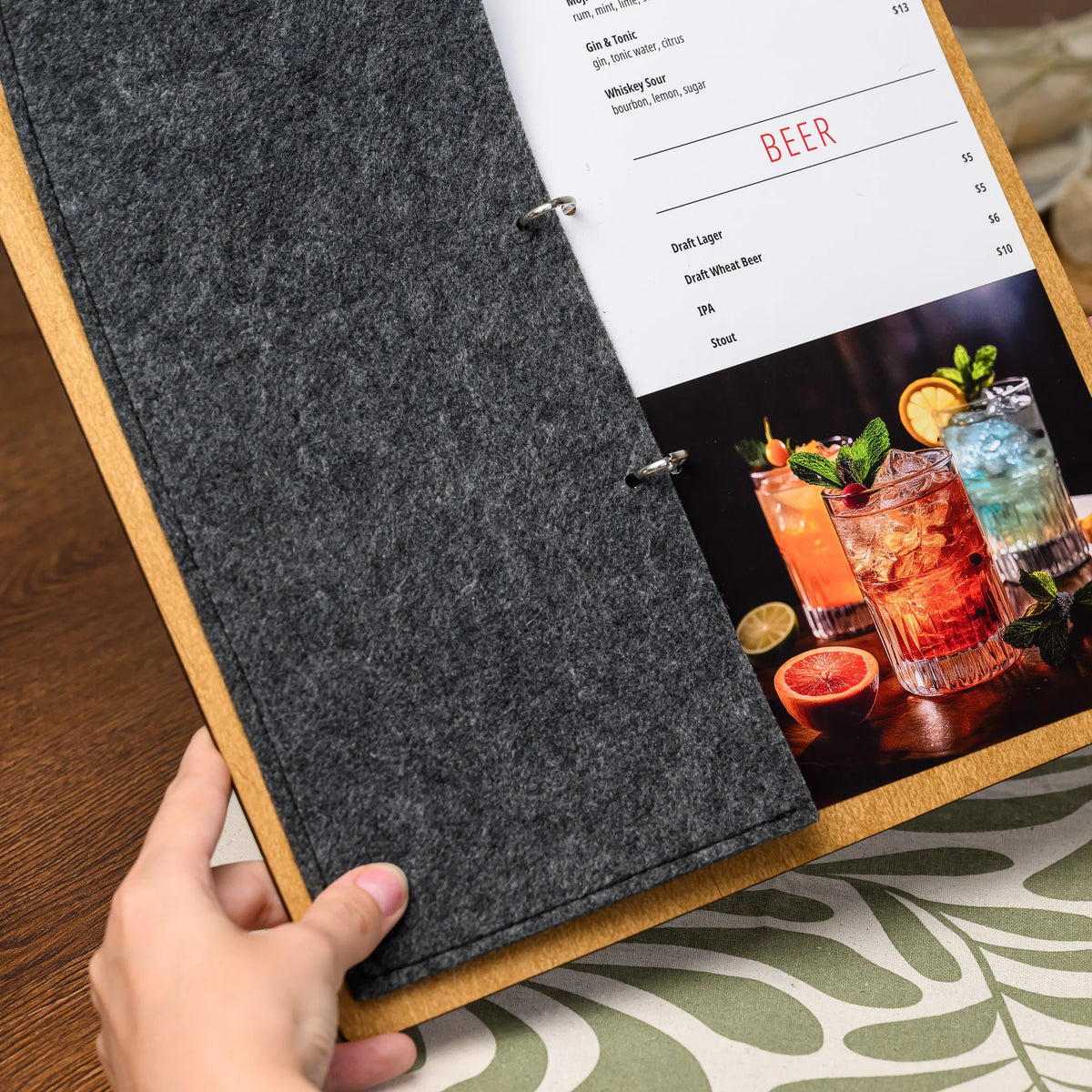 Фанерний планшет для винної карти з фетровою обкладинкою у руках, фетр відгорнутий, аркуш меню закріплений на кільцевому механізмі