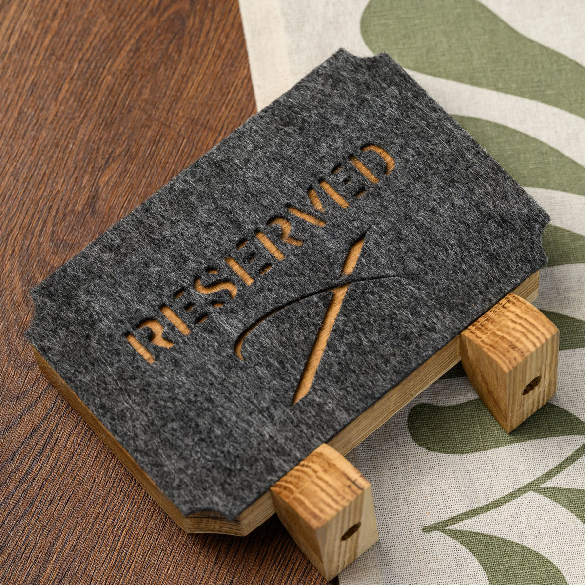 Дубова табличка «Reserved» з прорізаним фетром, лежить на столі: напис і символ прорізані до дерева, опори з отворами для кріплення