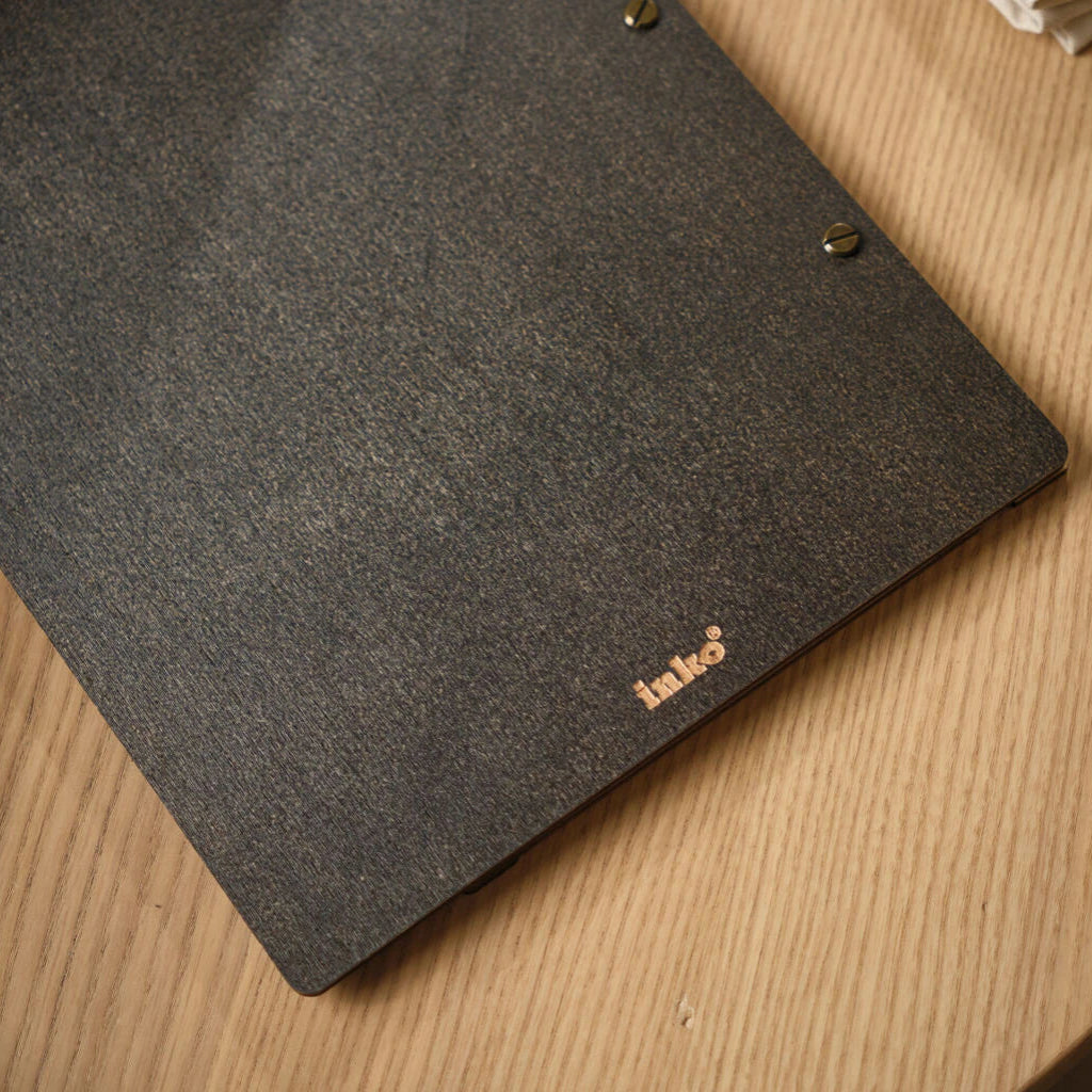 Macro detail of the dark Jeans-colored wood grain on the back of a menu folder, highlighting the elegant "inko" branding in gold