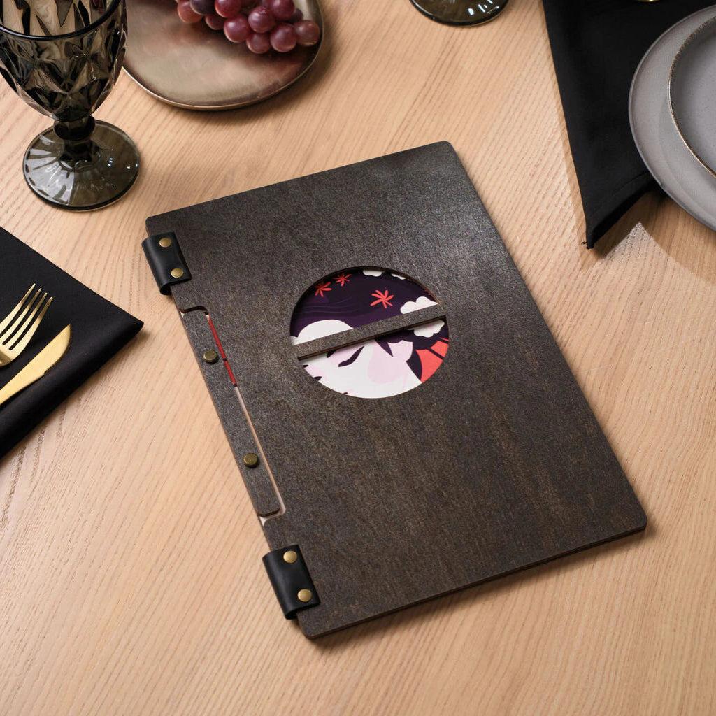 A closed dark wood menu folder with a circular cutout revealing an illustration of a Japanese geisha, set against a laid table.