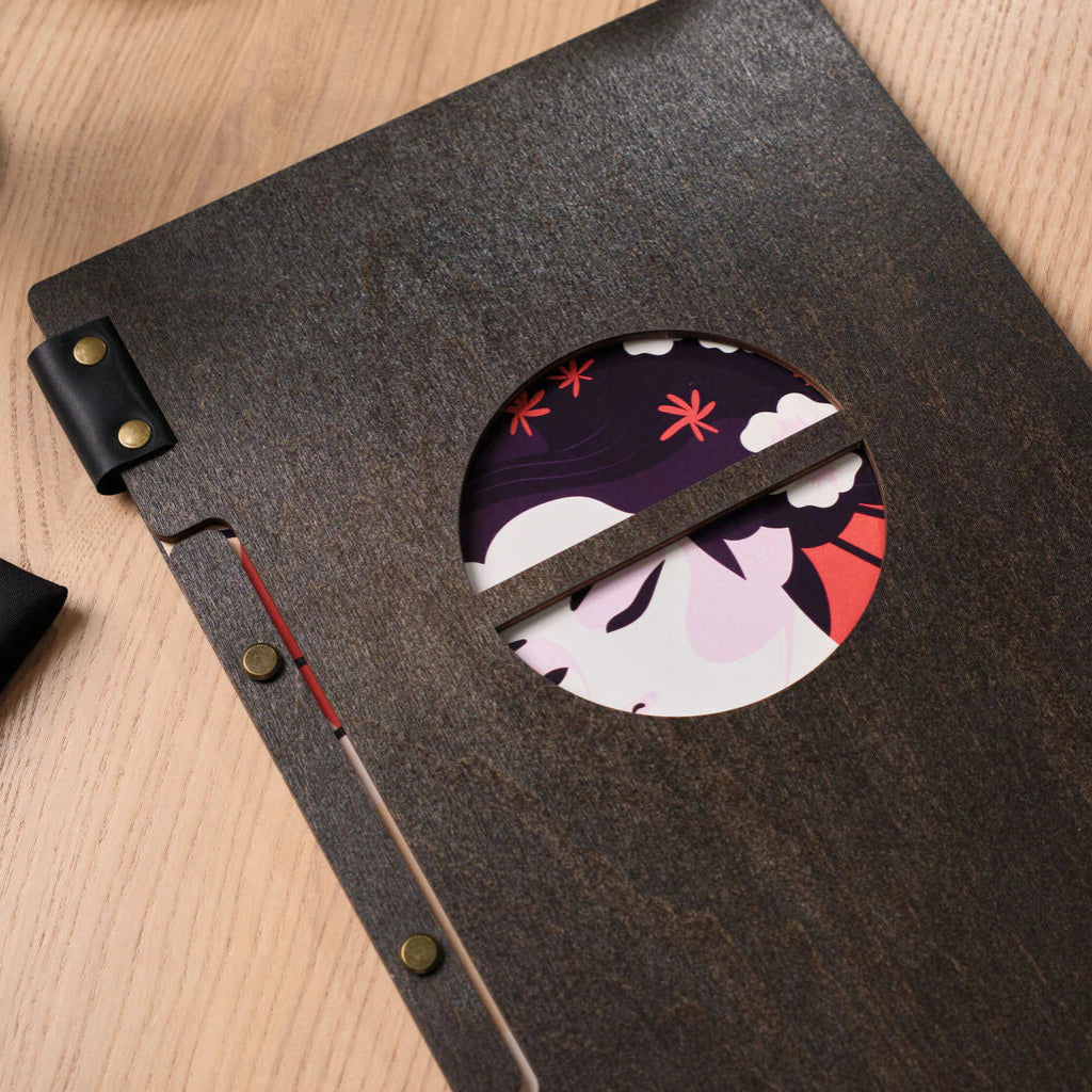 A close-up of a wooden menu folder's binding with brass screws and a circular cutout revealing illustration details.