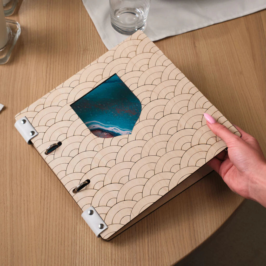 Top-down view of a customer pointing at a menu item inside a handcrafted wooden binder at a restaurant.